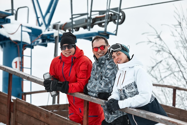 Zdjęcie grupa przyjaciół narciarzy na górze odpoczywa i pije kawę z termosu na tle wyciągu narciarskiego.