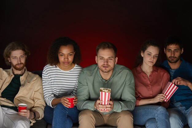 Grupa Przyjaciół Ogląda Filmy W Domu Jedząc Przekąski I Popcorn, Siedząc Na Dużej Kanapie W Ciemnym Pokoju