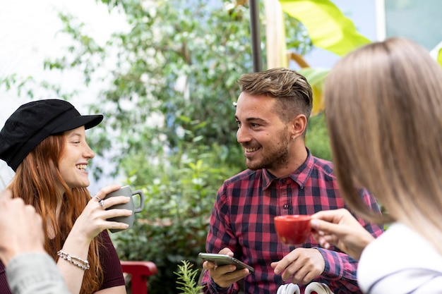 Grupa przyjaciół pije cappuccino w kawiarni Ludzie rozmawiają i bawią się razem w ogrodzie kawiarni Koncepcja przyjaźni ze szczęśliwymi chłopakami i dziewczynami w kawiarni restauracji Skupić się na twarzy mężczyzny