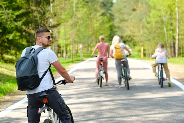 Grupa rowerzystów z plecakami jeździ na rowerach leśną drogą ciesząc się przyrodą.