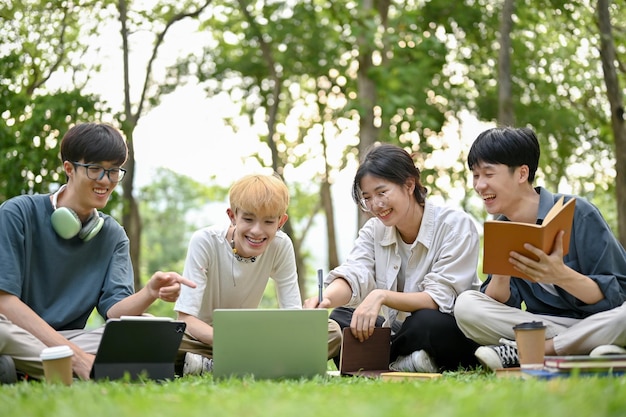 Grupa różnorodnych młodych azjatyckich studentów siedzących na trawie lubi rozmawiać w parku