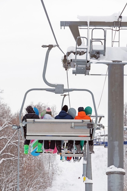 Grupa snowboardzistów wspina się na górę wyciągiem narciarskim aktywne ferie zimowe w ośrodkach narciarskich widok od tyłu