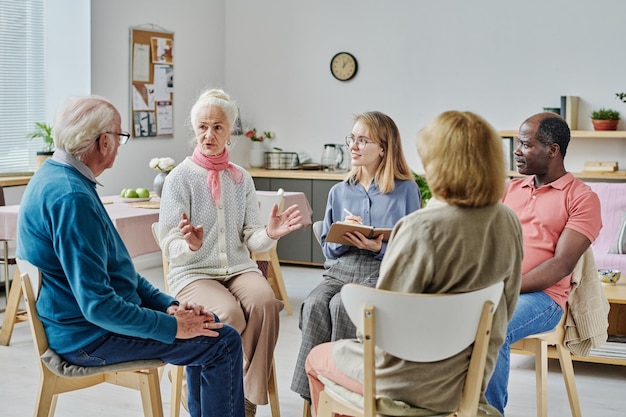 Grupa starszych osób siedzących na krzesłach i rozmawiających ze sobą podczas sesji psychoterapii