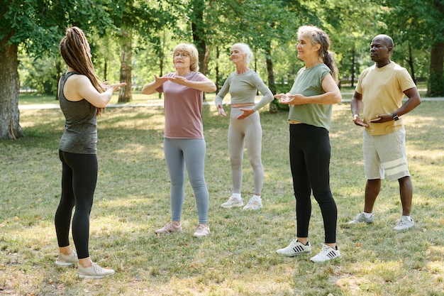 Zdjęcie grupa starszych osób wykonujących ćwiczenia oddechowe wraz z trenerem na świeżym powietrzu