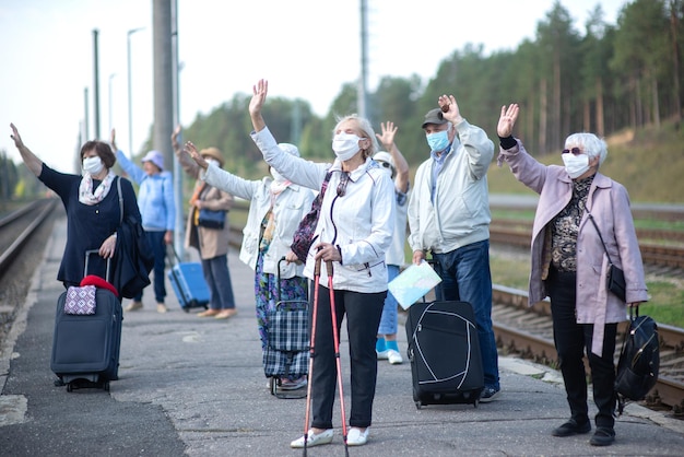 Grupa starszych przyjaciół w maskach na peronie czeka na pociąg