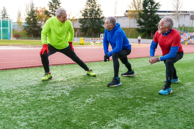 Zdjęcie grupa starszych sportowców w strojach sportowych wykonuje rozciągania boczne na torze biegowym