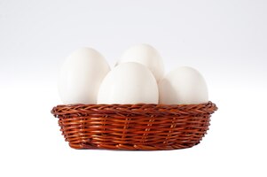 Grupa świeżych białych jaj kurzych w mini brązowym koszyku wiklinowym na białym tle, odizolowane
