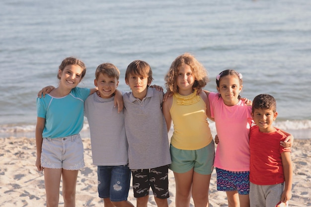 Zdjęcie grupa szczęśliwych dzieci bawiących się na plaży, przytulających się i uśmiechających się patrząc w obiektyw dzieci cieszące się letnimi wakacjami z przyjaciółmi