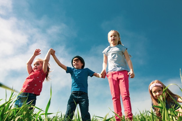 Grupa szczęśliwych dzieci chłopców i dziewczynek biega po parku po trawie w słoneczny letni dzień Pojęcie przyjaźni etnicznej pokój życzliwość dzieciństwo
