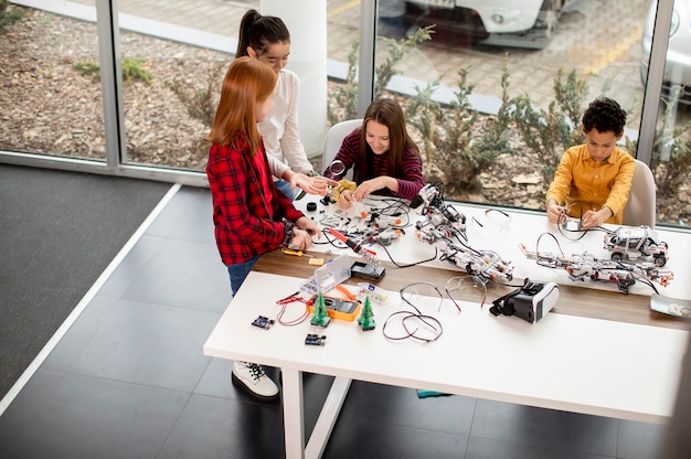 Zdjęcie grupa szczęśliwych dzieciaków programujących zabawki elektryczne i roboty w klasie robotyki