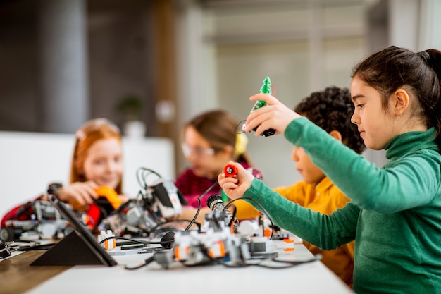 Grupa szczęśliwych dzieciaków programujących zabawki elektryczne i roboty w klasie robotyki