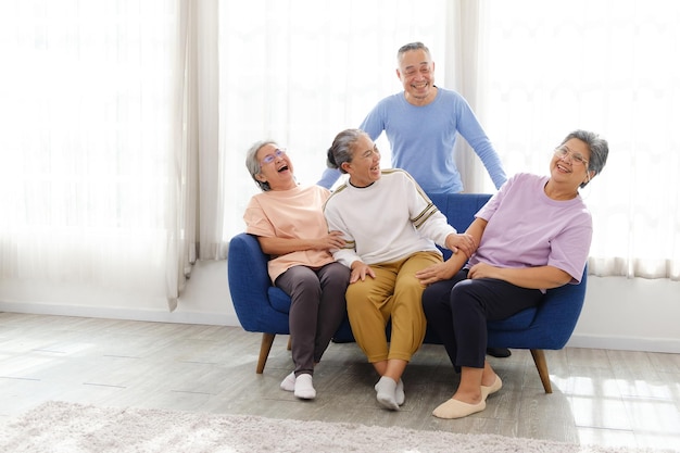Grupa szczęśliwych i zdrowych trzech azjatyckich starszych kobiet siedzi razem na kanapie z azjatyckim starszym mężczyzną stojącym z tyłu, uśmiechając się i śmiejąc razem Obraz z kopią miejsca