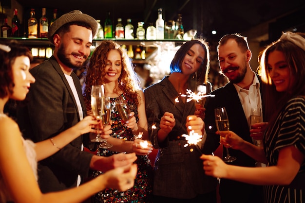 Grupa szczęśliwych ludzi posiadających zimne ognie na imprezie. Młodzi przyjaciele brzęk kieliszków szampana.