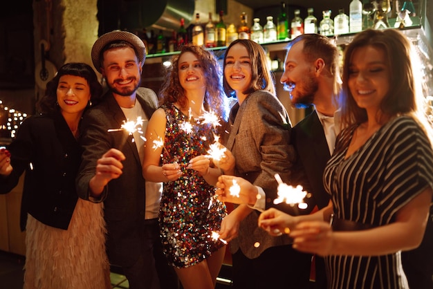 Grupa szczęśliwych ludzi posiadających zimne ognie na imprezie. Młodzi przyjaciele brzęk kieliszków szampana.