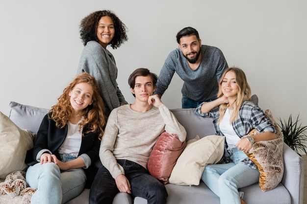 Grupa szczęśliwych młodych przyjaciół międzykulturowych w casualwear relaks na miękkiej kanapie razem w izolacji