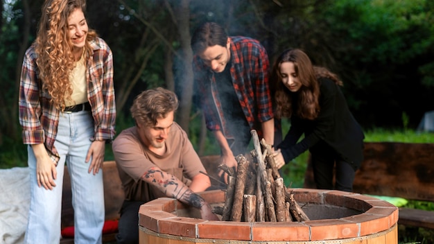 Grupa szczęśliwych młodych przyjaciół próbujących rozpalić ognisko w glampingu. Dwóch mężczyzn i kobiet