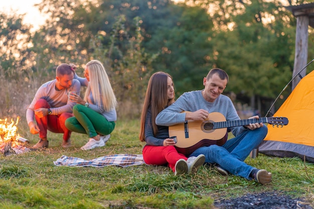 Grupa Szczęśliwych Przyjaciół Z Gitarą, Zabawy Na świeżym Powietrzu, W Pobliżu Ogniska I Namiotu Turystycznego. Zabawa Na Kempingu Szczęśliwa Rodzina