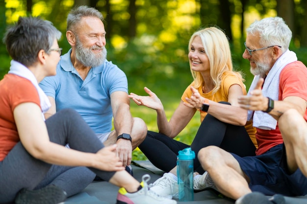 Zdjęcie grupa szczęśliwych seniorów odpoczywających razem po treningu fitness w parku