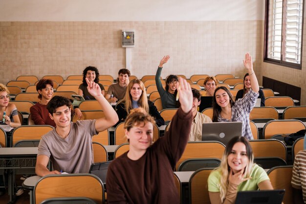 Grupa uczniów w klasie podnosi ręce, aby odpowiedzieć na pytania, skupia się na dziewczynie w drugiej linii