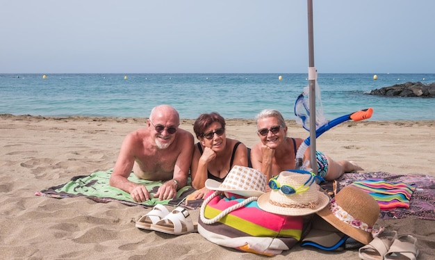 Grupa uśmiechniętych seniorów kaukaski leżący na plaży nad morzem, ciesząc się wolnym czasem szczęśliwe dojrzałe kobiety i mężczyzna patrząc na kamery