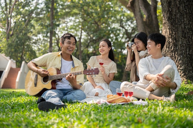 Grupa wesołych, zróżnicowanych młodych przyjaciół z Azji cieszy się razem piknikem w pięknym parku