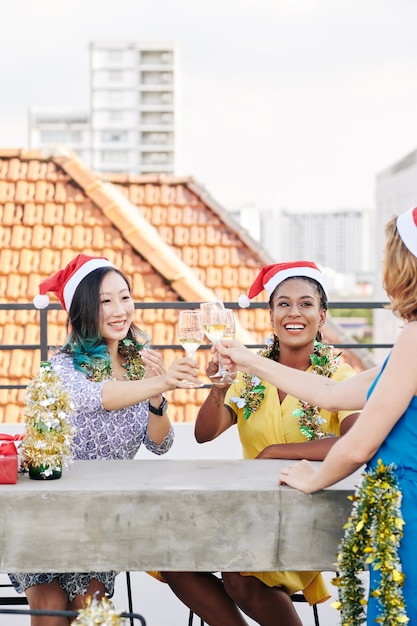 Grupa wieloetnicznych młodych kobiet świętujących Boże Narodzenie i wznoszących toast kieliszkami szampana