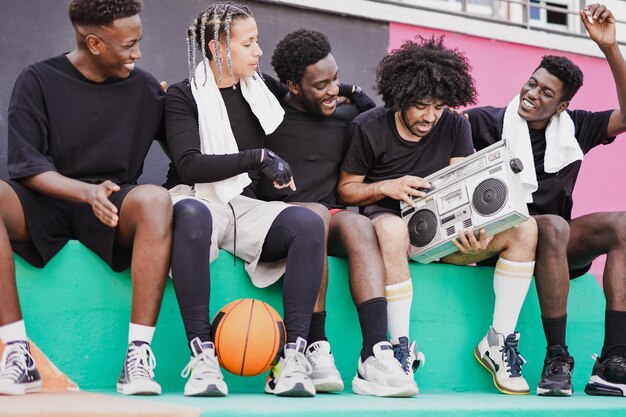 Zdjęcie grupa wieloetnicznych przyjaciół bawiących się z vintage boomboxem po meczu koszykówki w mieście