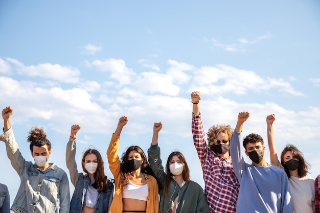 Grupa wielorasowych demonstrantów z pięściami uniesionymi w powietrzu, noszących maskę ochronną Aktywiści protestujący na ulicy Kopiowanie przestrzeni Koncepcja demonstracji