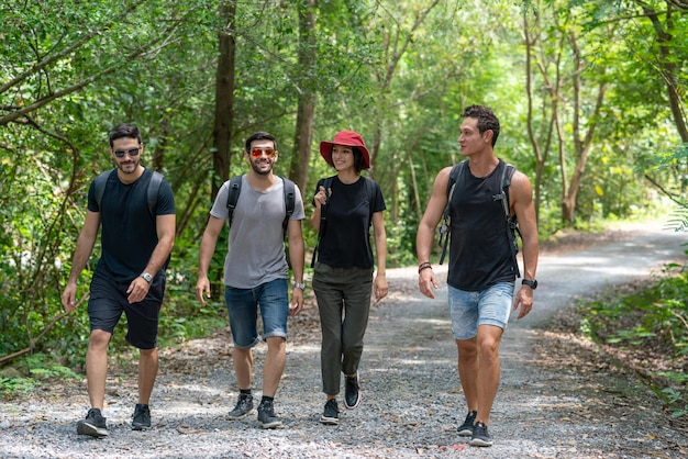 Grupuj przyjaciół z plecakami podróżujących i wędrujących razem w leśnej przyrodzie w wakacyjnym lecie
