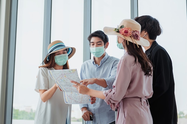 Grupy Turystów Noszą Maski I Oglądają Mapy Na Lotnisku Przed Podróżą.