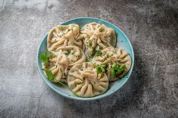 Gruzińskie pierożki chinkali z mięsem, zieleniną i pikantnym sosem pomidorowym Satsebeli na tle szarego kamiennego stołu