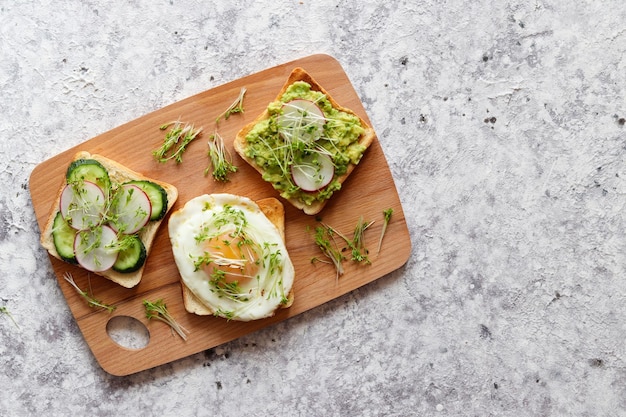 Grzanki lub bruschetta z jajkiem, ogórkiem, rzodkiewką, awokado i microgreens na stole Smaczne śniadanie