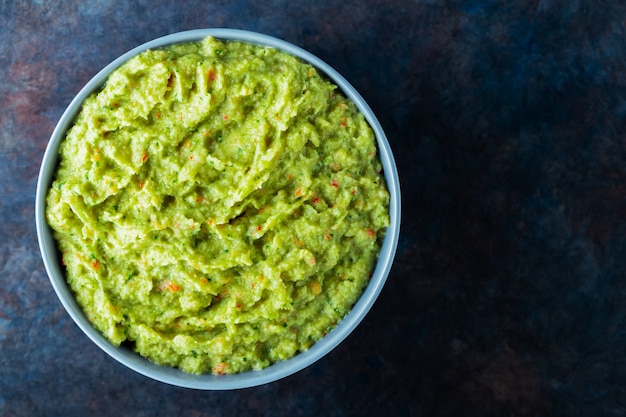 Guacamole w szarej misce na ciemnym tle. Miska sosu guacamole z awokado ze świeżymi składnikami. Skopiuj miejsce. Widok z góry