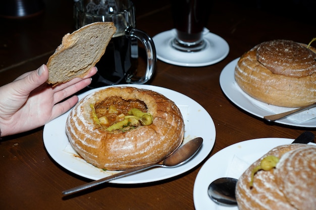 Gulasz Podawany W Misce Chlebowej Na Białym Talerzu. Restauracja W Czechach. Kuchnia Czeska. Ręka Podnosi Pokrywkę Chleba