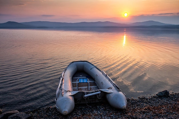 Gumowa łódź na brzegu malowniczego wybrzeża na tle wschodu słońca