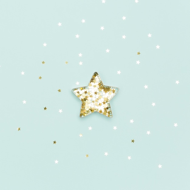 Gwiazda bożonarodzeniowa wykonana z formy do ciastek i złotych błyszczących gwiazd na niebieskim tle Płaska świeca