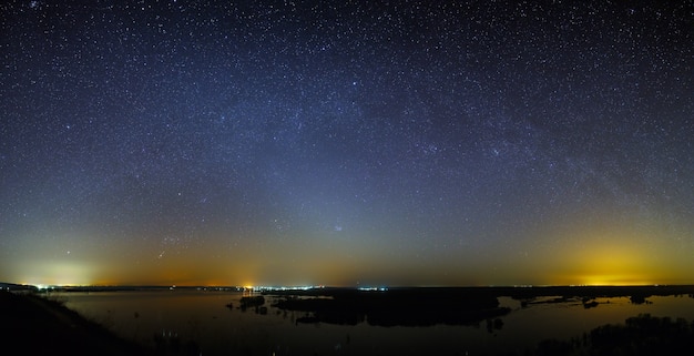 Gwiazdy Drogi Mlecznej na niebie przed świtem. Nocny krajobraz z jeziorem. Panoramiczny widok na gwiaździstą przestrzeń.