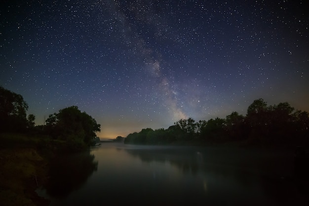 Gwiaździste nocne niebo z Drogą Mleczną nad rzeką.