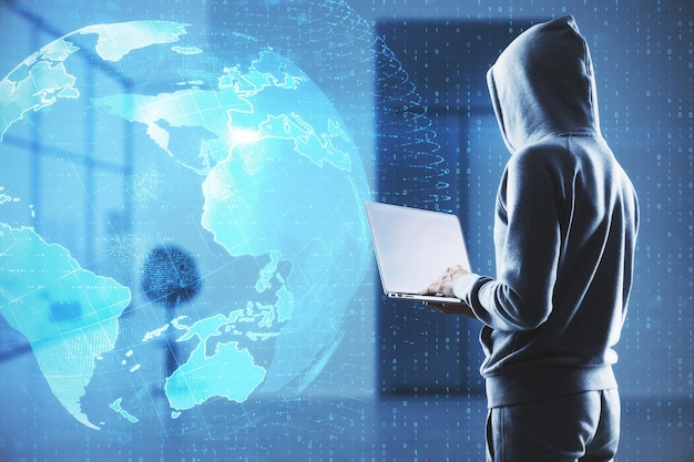 Haker w rozmytym wnętrzu biurowym za pomocą laptopa z kreatywnym, świecącym interfejsem kuli ziemskiej na ciemnym tle Sieć technologiczna hakująca kradzież i koncepcja danych online