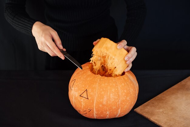 Halloween, Ręce dziewczyny z nożem do cięcia pomarańczowej dyni do robienia latarni Jacka