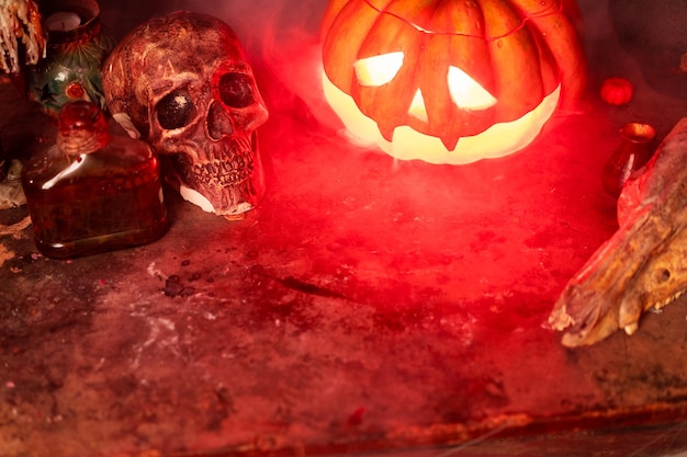 Halloween. Straszna dynia Halloween z rzeźbioną twarzą na stole w ciemnym pokoju z ludzką czaszką i zwierzęcą czaszką. Skopiuj miejsce na tekst. Upiorna atmosfera.