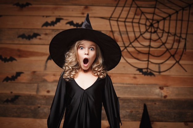 Halloween Witch Koncepcji - Przeznaczone Do Walki Radioelektronicznej Strzału Niewiele Kaukaski Czarownica Dziecko Szoku Twarzy Stwarzających Z Bat I Pajęczyna Sieci Web Na Tle Drewniane Studio.