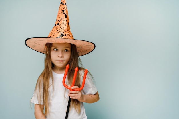 Zdjęcie halloweenowa dziewczyna dla dzieci wygłupia się z małym diabłem trójzębem na niebieskim tle z miejscem na kopię gotowa na weekend z żartami lub smakołykami