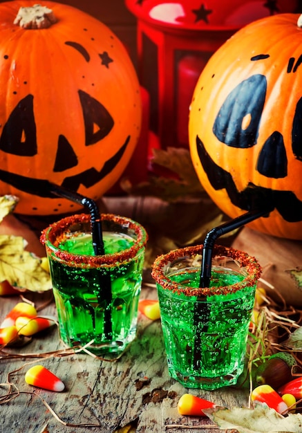 Halloweenowa Kompozycja Ze świątecznym Zielonym Napojem I Uśmiechniętymi Dyniami Do Picia Ze Słomą Kukurydzy I Opadłymi Liśćmi Na Ciemnym Tle Selektywna Ostrość