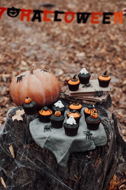 Zdjęcie halloweenowe babeczki i świąteczny wystrój na liściach klonu wśród drzew w sezonie jesiennym na świeżym powietrzu