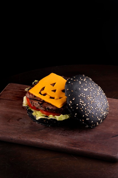 Halloweenowy burger z zabawnym serem cheddar i czarną bułką z gergiliną na ożypałce i ciemnym tle