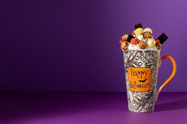 Halloweenowy Freak Shake W Wysokim Kubku Na Fioletowym Tle Z Cieniem. Bita śmietana Z Glazurowanym Popcornem, Kolorową Pianką I Czekoladą. Tło Halloween Z Miejsca Na Kopię.