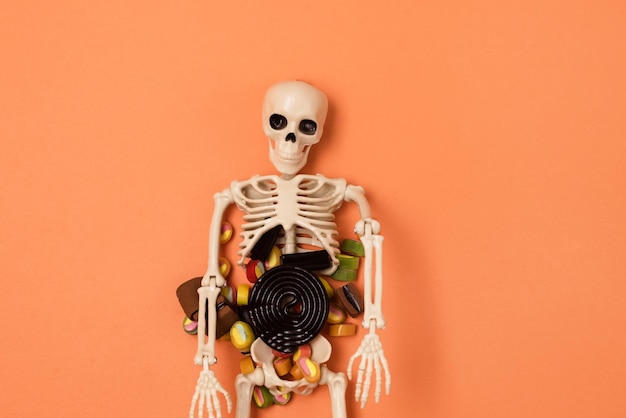 Halloweenowy szkielet z świątecznymi cukierkami i słodyczami na pomarańczowym tle Halloween