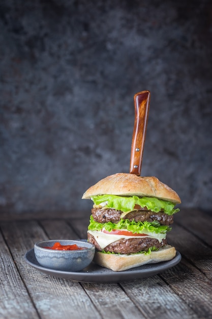 Hamburger z burgerem mięsnym wołowym i świeżymi warzywami na ciemnym tle. Smaczne fast foody.