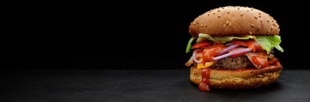 Hamburger z keczupem z pomidorami wołowymi i cebulą na czarnym tle z miejscem na tekst selektywne focus